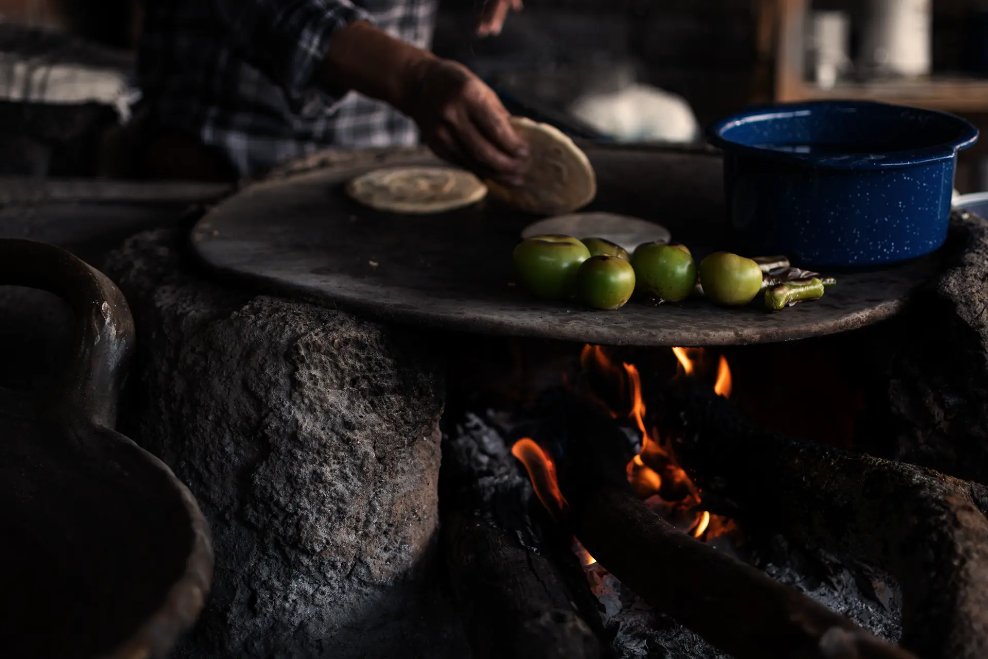 Hands turning handmade corn tortillas on a comal over a wood fire